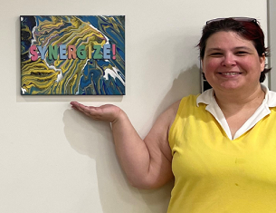 Ms. Denny, the Media Specialist beside a small canvas with the word "Synergize" on it.