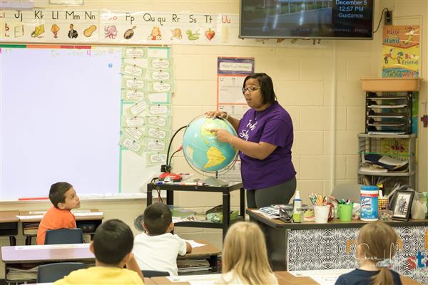 teacher pointing to globe and students in desks watching