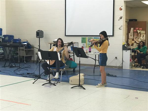 Student sitting playing guitar and student standing playing violin