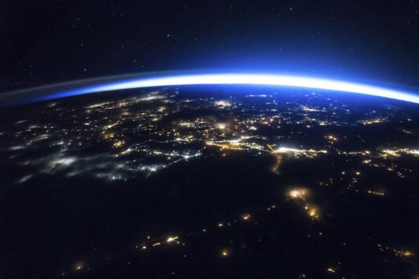 Image of the earth from outer space, looking at the side of the planet experiencing night time, with city lights on the ground lighting up parts of the dark surface.